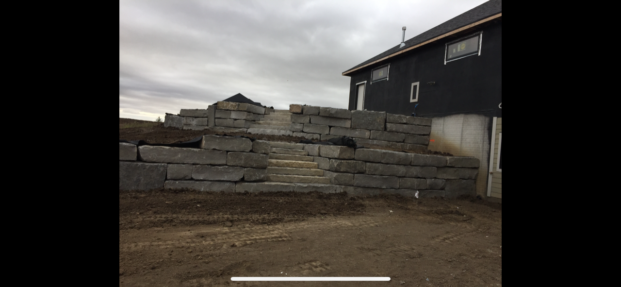 A large stone wall is being built in front of a house.