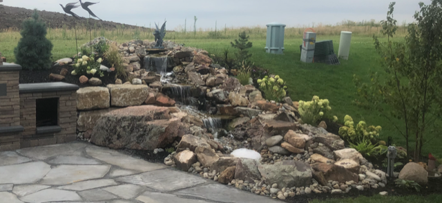 There is a waterfall in the middle of the rocks in the backyard.