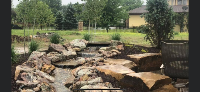 A waterfall is surrounded by rocks and trees in a backyard.