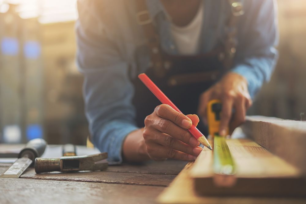 Person Measuring and Marking a Wooden Board With a Red Pencil in a Workshop — C K Carpentry in Byron Bay, NSW