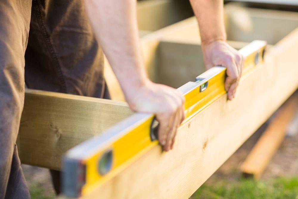 Hands Using a Yellow Level to Align Wooden Boards During Outdoor Construction — C K Carpentry in Byron Bay, NSW