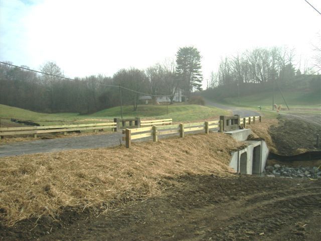 A wooden fence surrounds a dirt road in a field.
