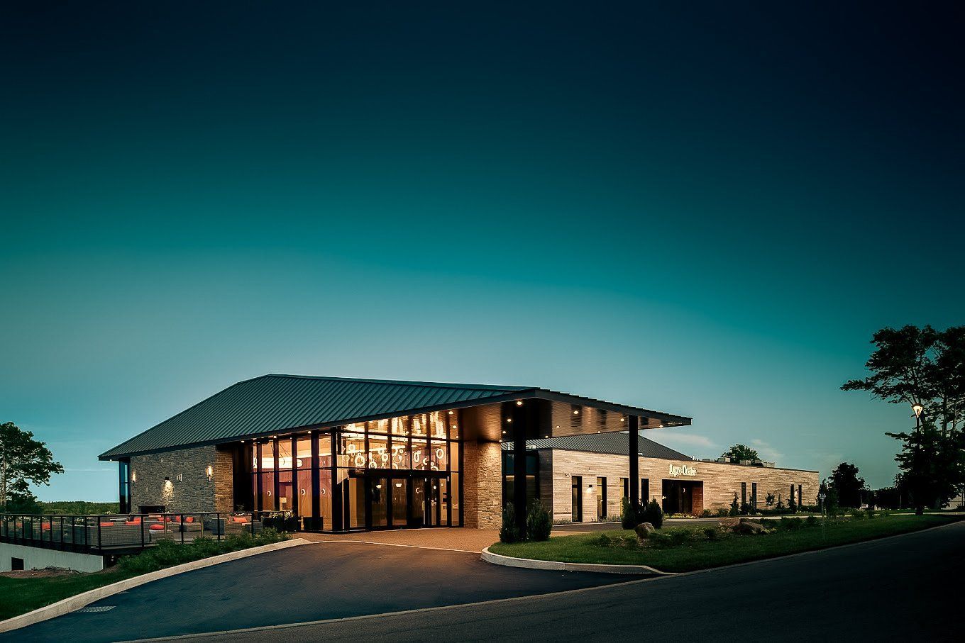 Modern stone building with glass entrance, dark roof, and surrounding landscaping.
