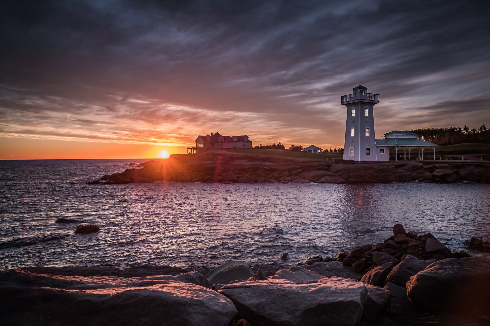 Lighthouse on rocky coast at sunset, with golden light reflecting in the water.