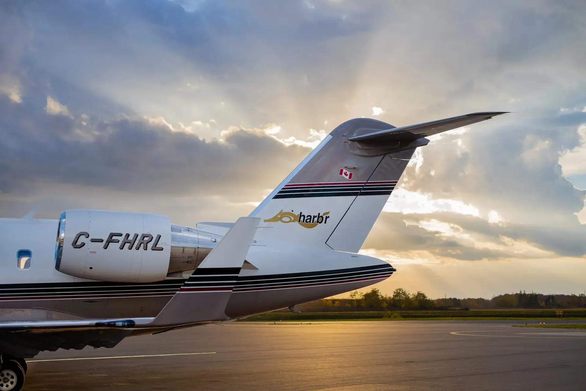 Tail of a white and silver private jet on a tarmac; sunlit clouds in the background.