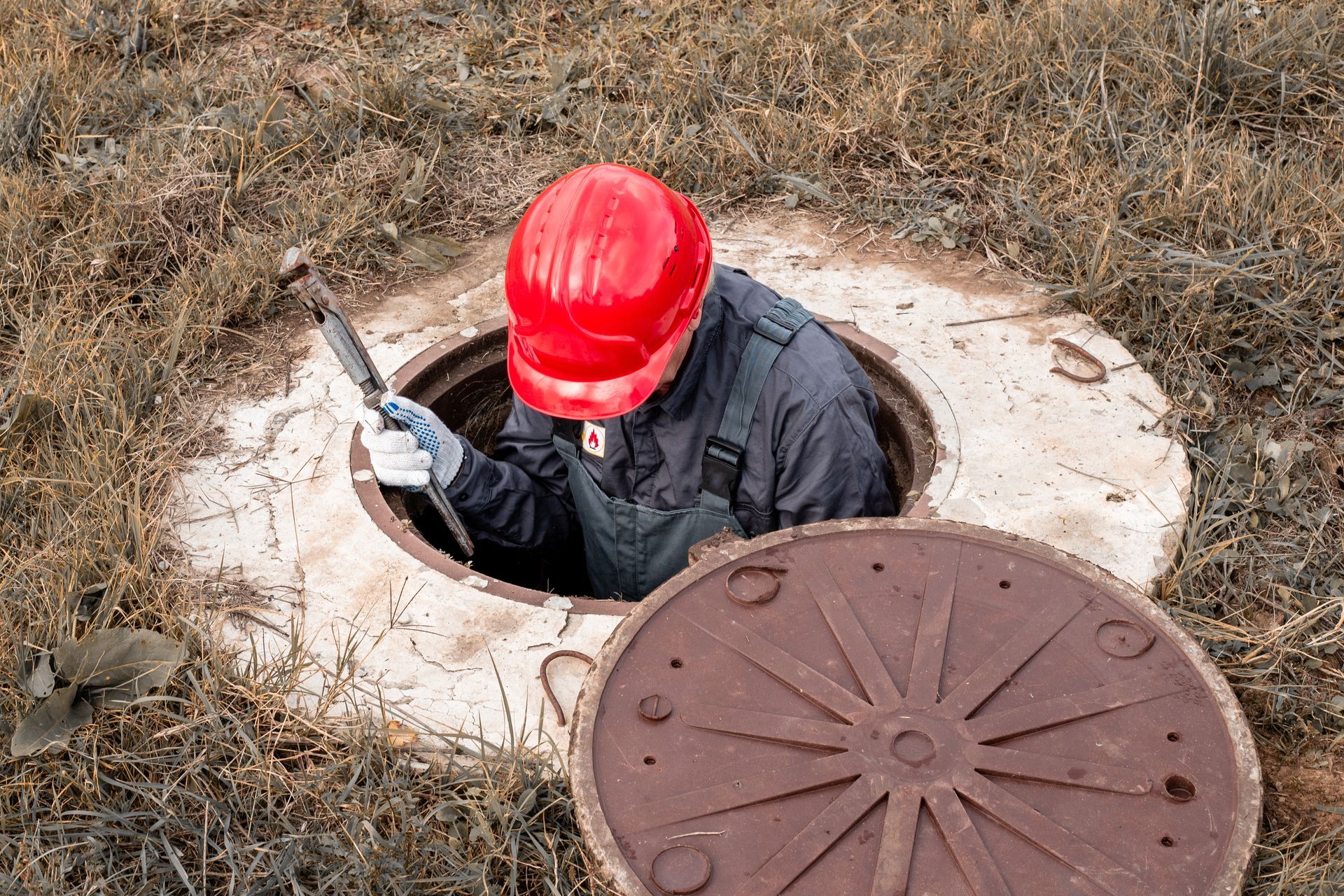 A worker in a helmet sits in a water well with an adjustable wrench.