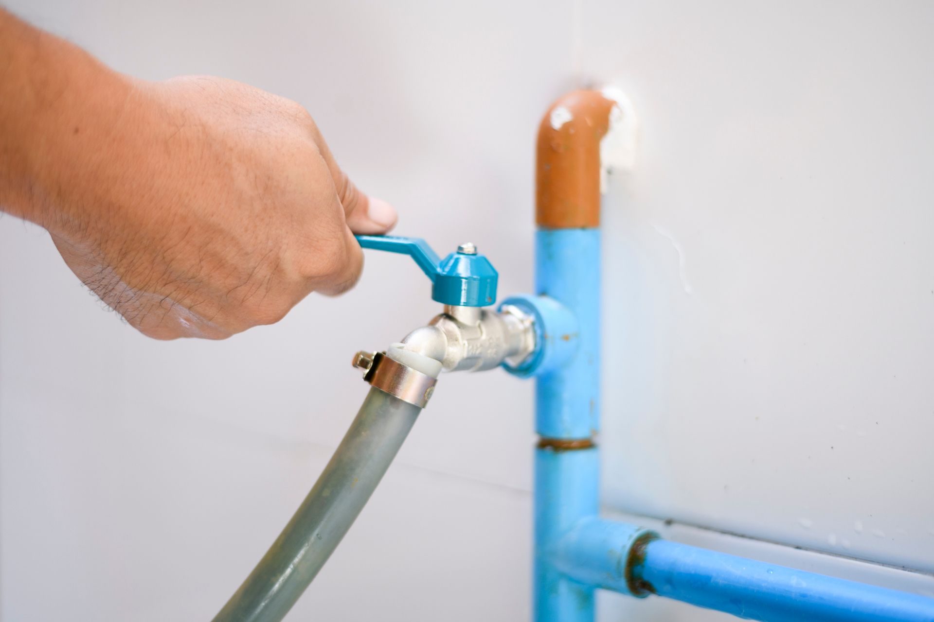 A hand opens the blue faucet of a blue pipe.