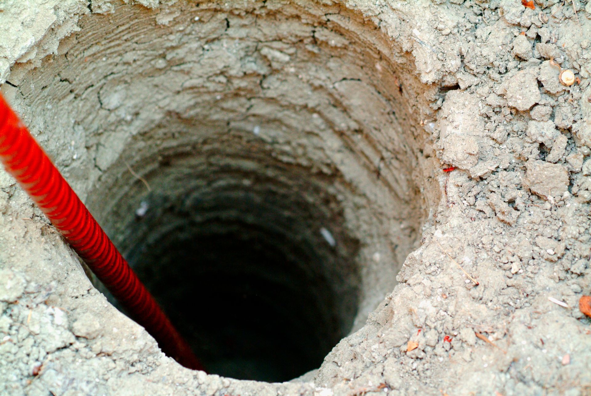 A hole in the ground with a red hose sticking out of it.