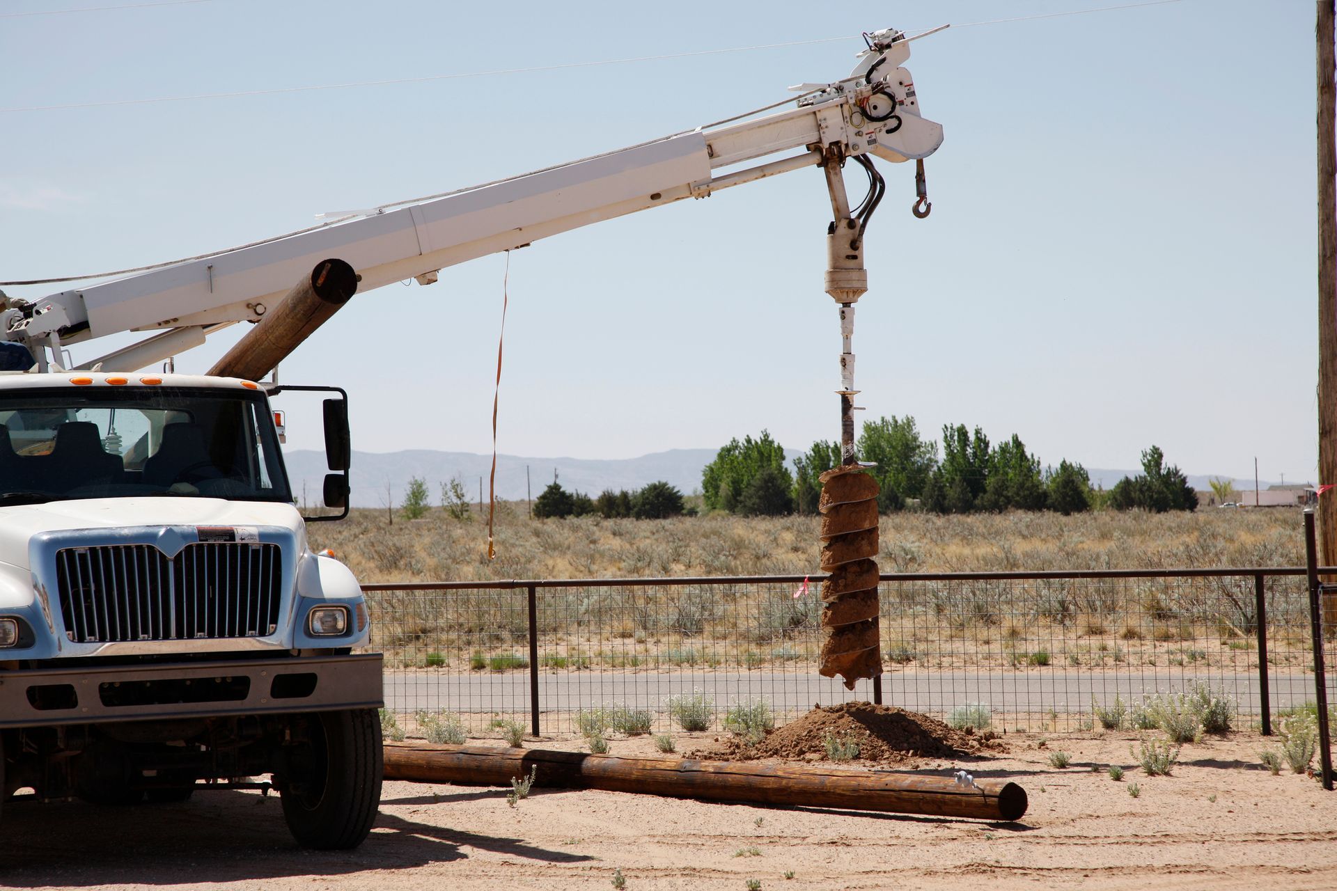 A white truck with a crane attached to it is parked in a field.