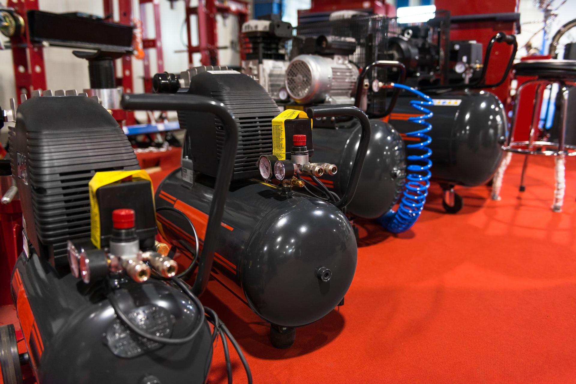 Industrial air compressors on display with pressure gauges and coiled blue hose.