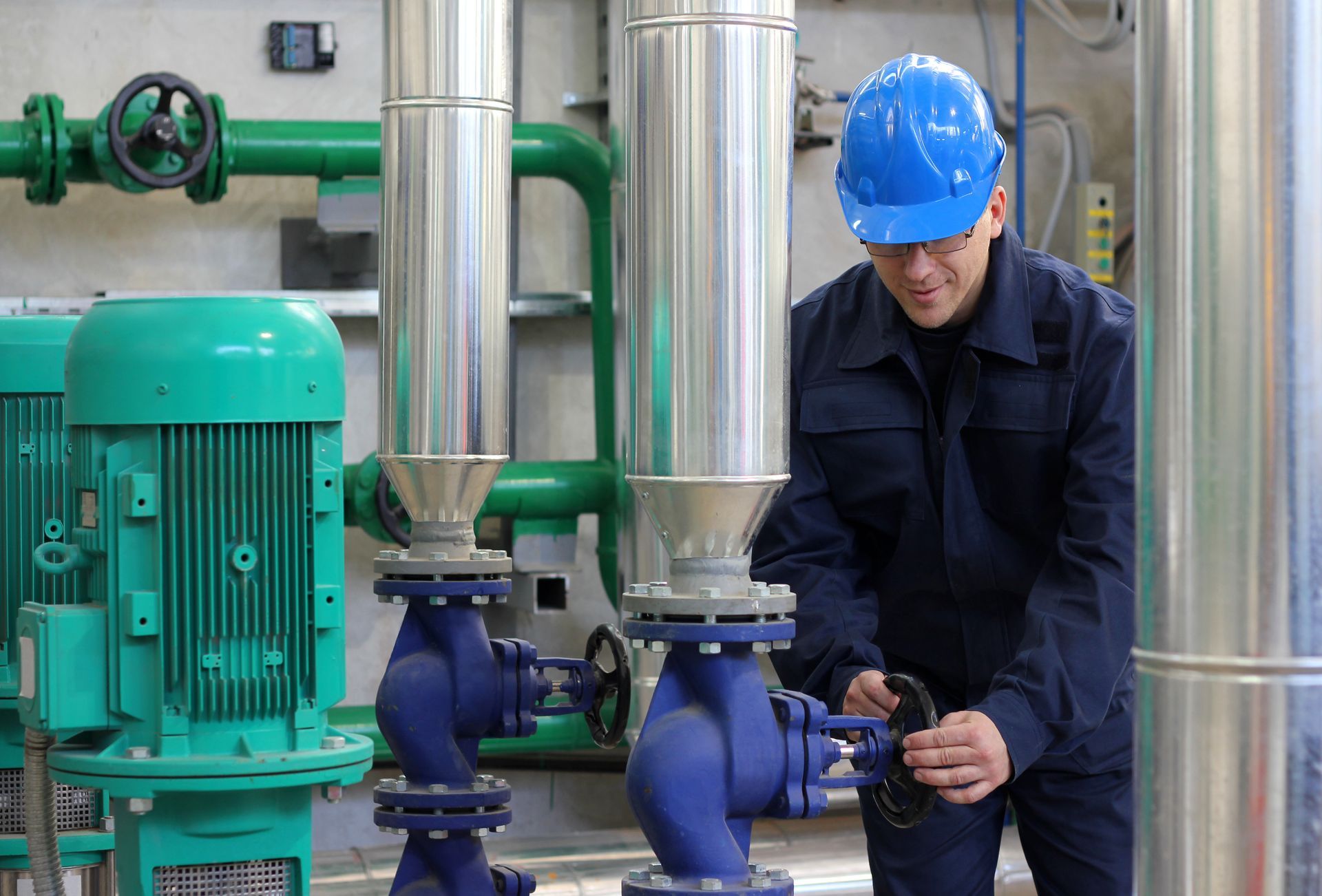Technician adjusting industrial water pump valves in a mechanical room with green pipes.