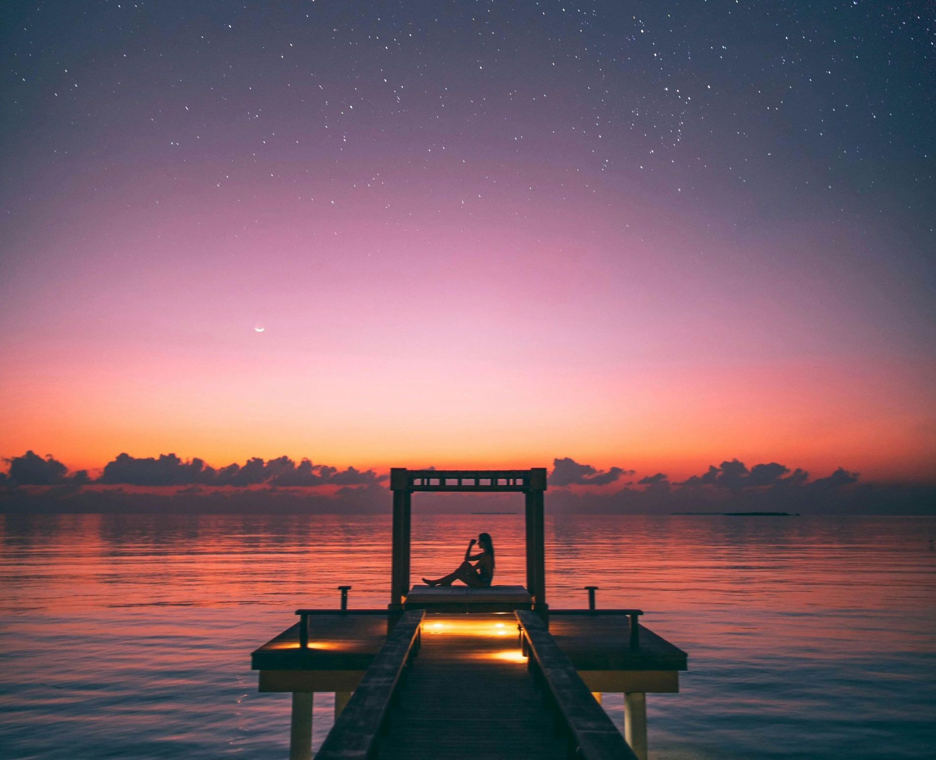 A couple is sitting on a dock overlooking the ocean at sunset.