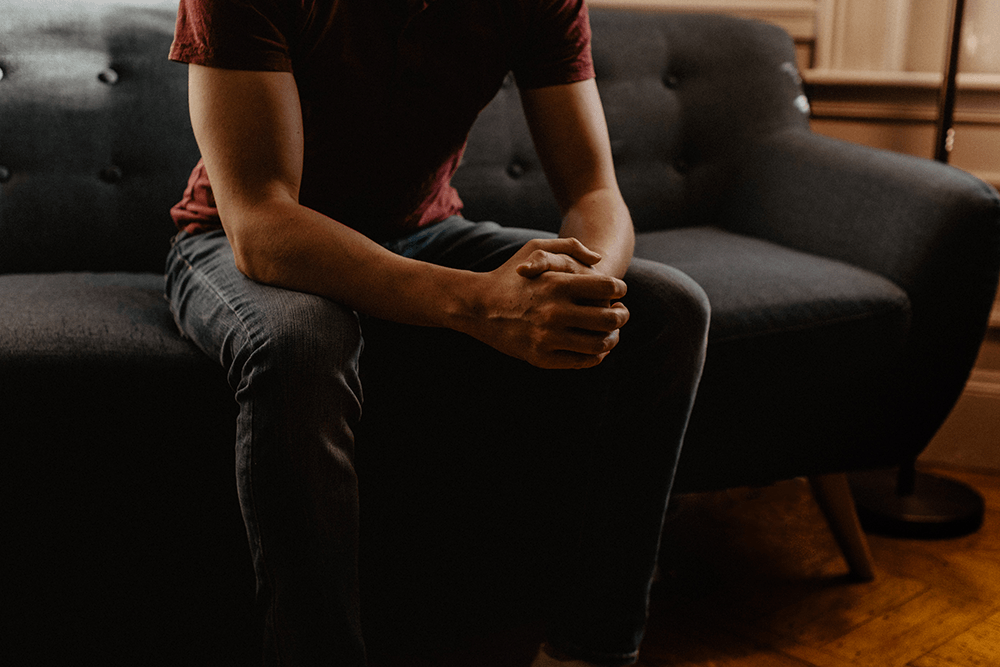 A man is sitting on a couch with his hands folded.