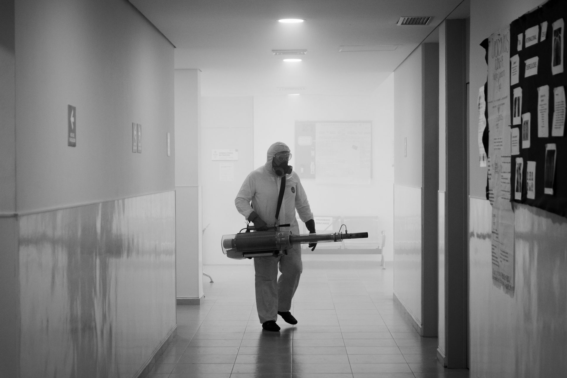Un homme en combinaison de protection pulvérise du désinfectant dans un couloir.