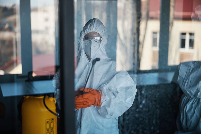 Un homme en combinaison de protection pulvérise une pièce avec un pulvérisateur.