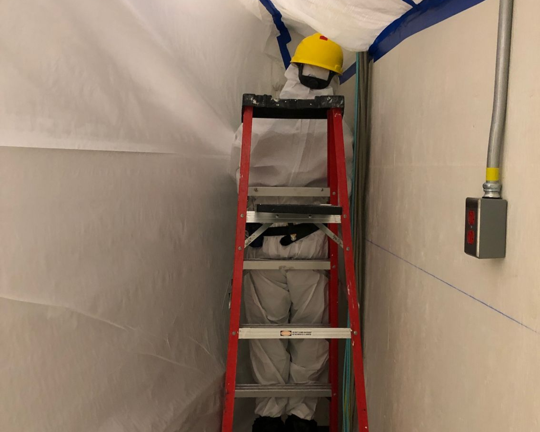 Un homme en combinaison de protection pulvérise une pièce avec un pulvérisateur.