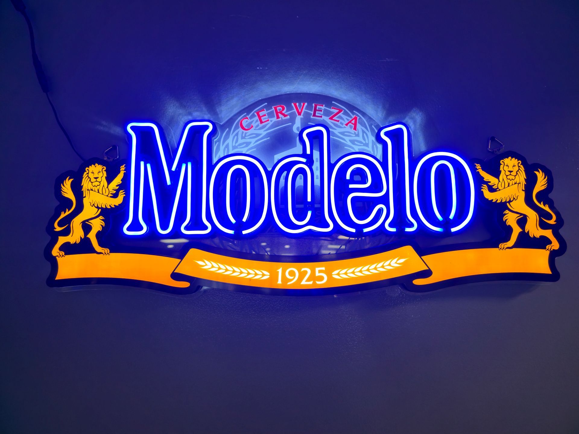 A neon blue Modelo beer sign with gold lions and a banner displaying 