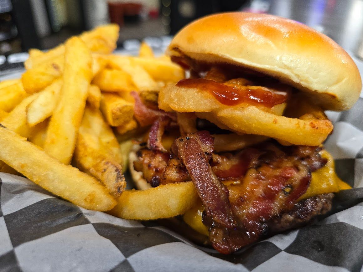 A group of people socializing at a bar with colorful cocktails and small appetizers lined up on the wooden counter.