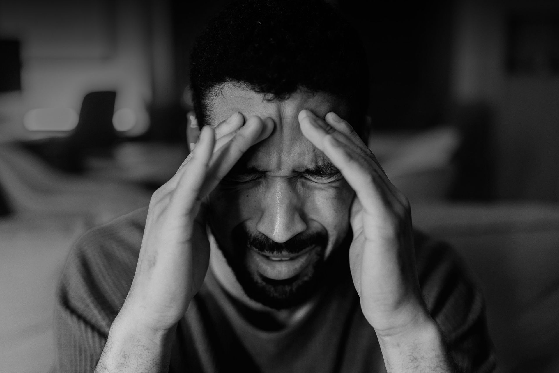 A man is holding his head in pain while sitting on a couch.