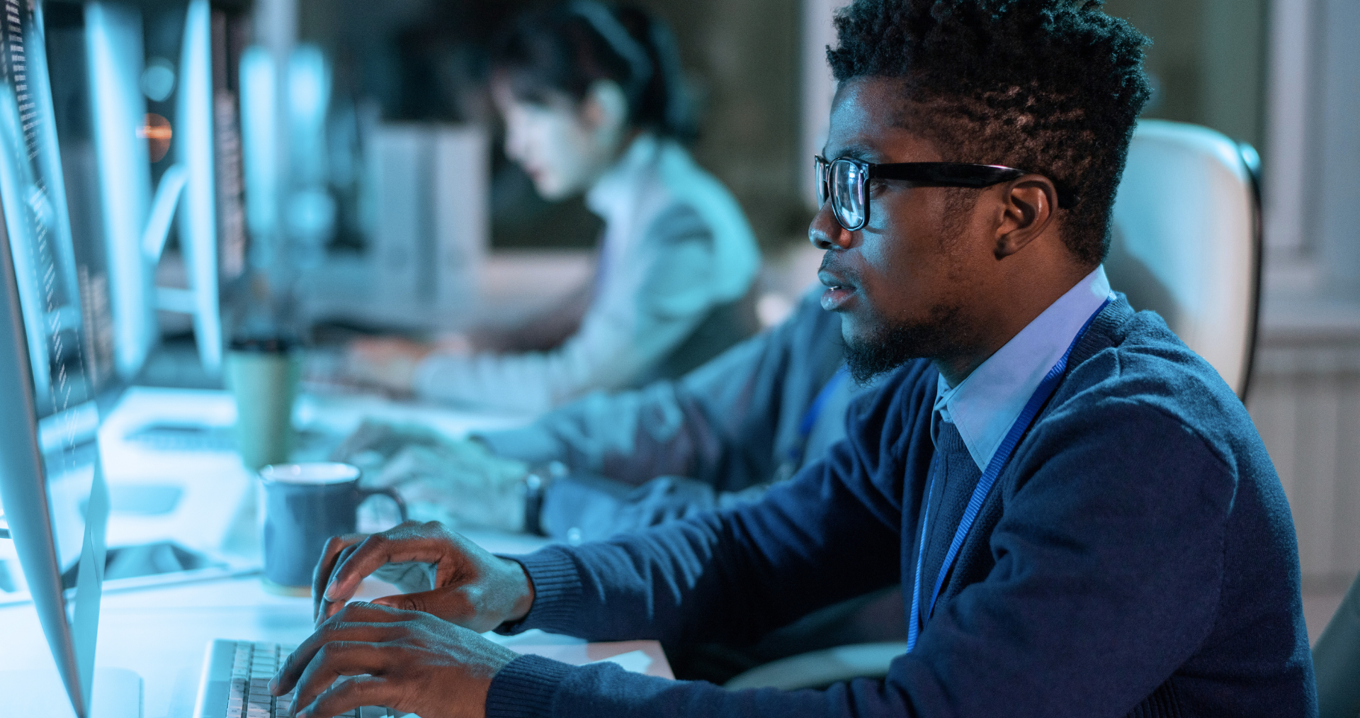 A man wearing glasses is typing on a computer keyboard.