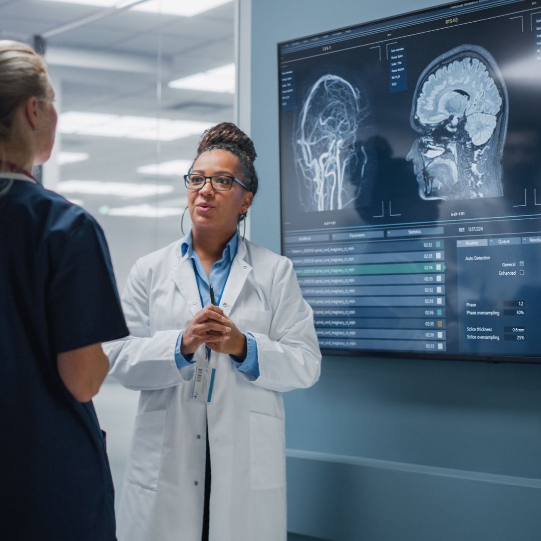 A female doctor is talking to a nurse in front of a large screen.