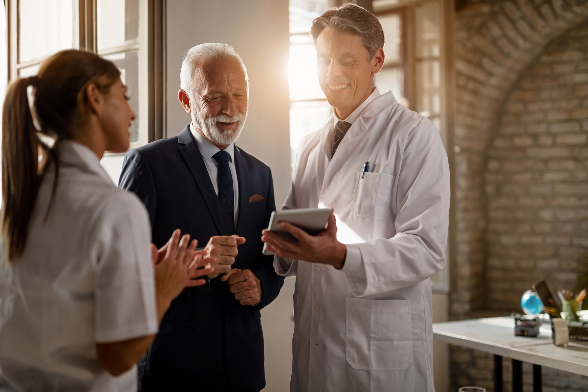 A group of doctors are talking to each other while a man in a suit looks at a tablet.