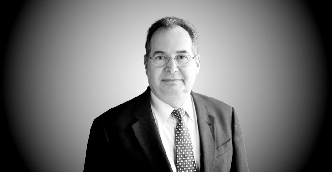 A man in a suit and tie is standing in front of a gray background.