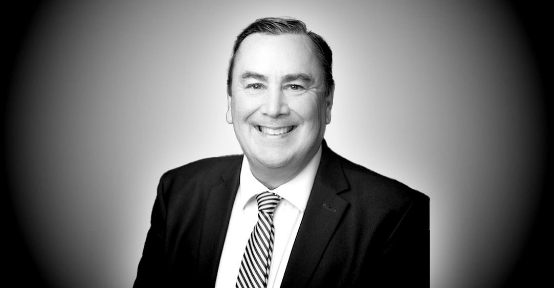 A man in a suit and tie is smiling in a black and white photo.