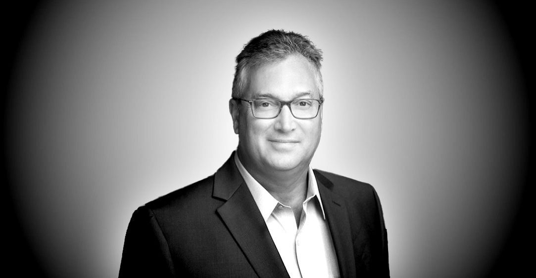 A man in a suit and glasses is smiling in a black and white photo.