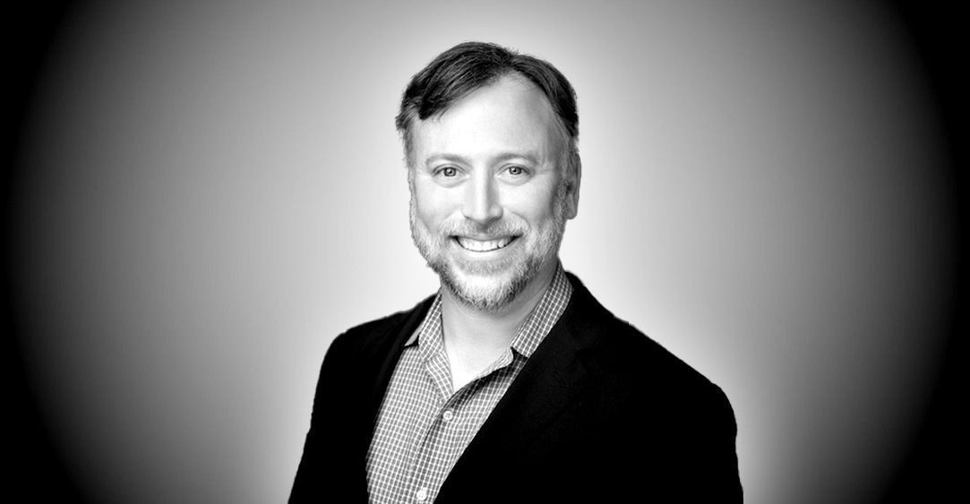 A man with a beard is smiling in a black and white photo.