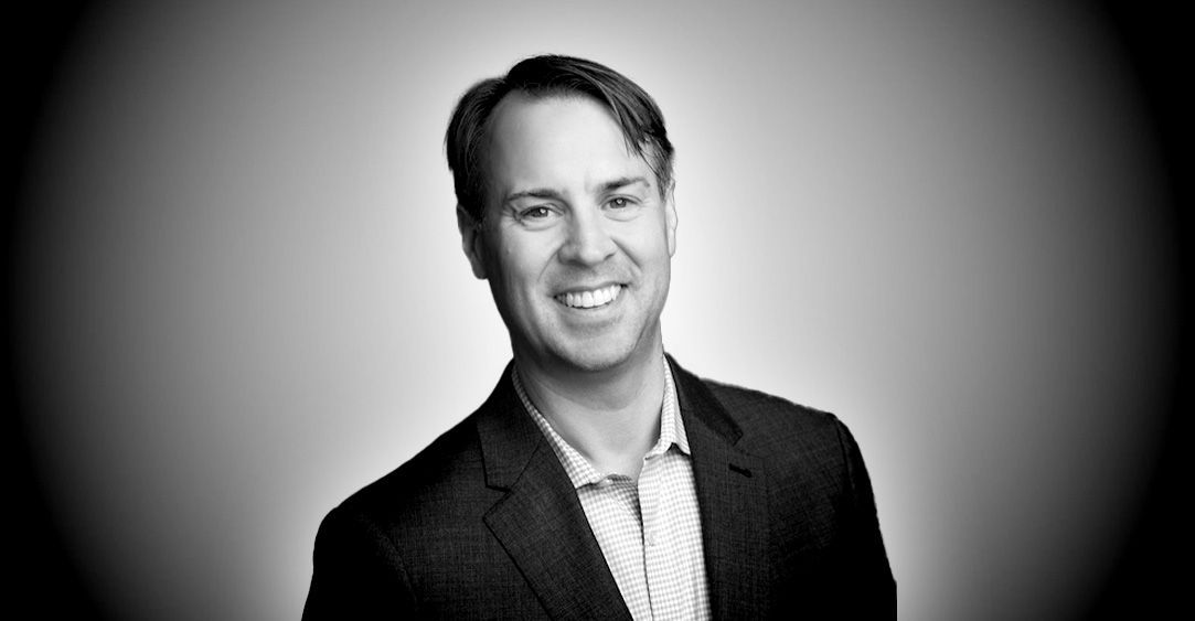 A man in a suit and striped shirt is smiling in a black and white photo.