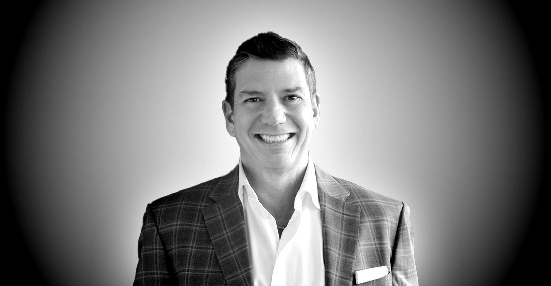 A man in a suit and white shirt is smiling in a black and white photo.