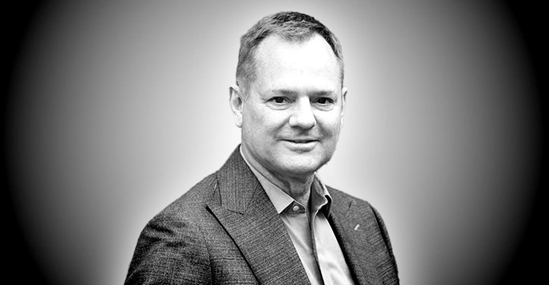 A man in a suit and tie is smiling in a black and white photo.