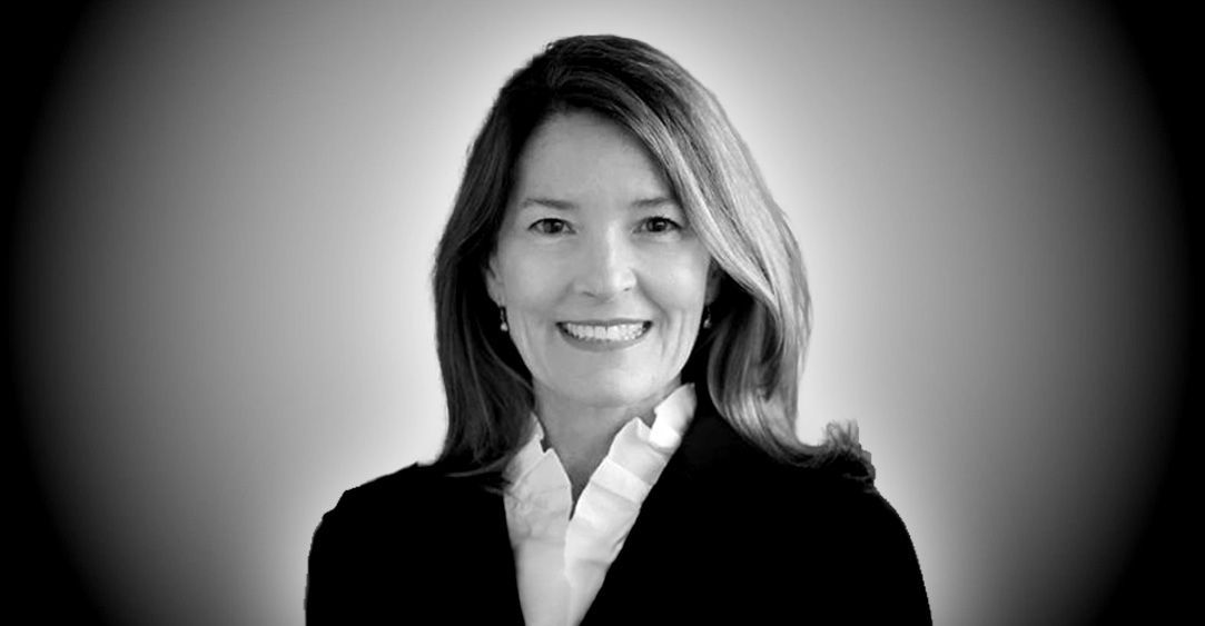 A woman in a suit and white shirt is smiling in a black and white photo.