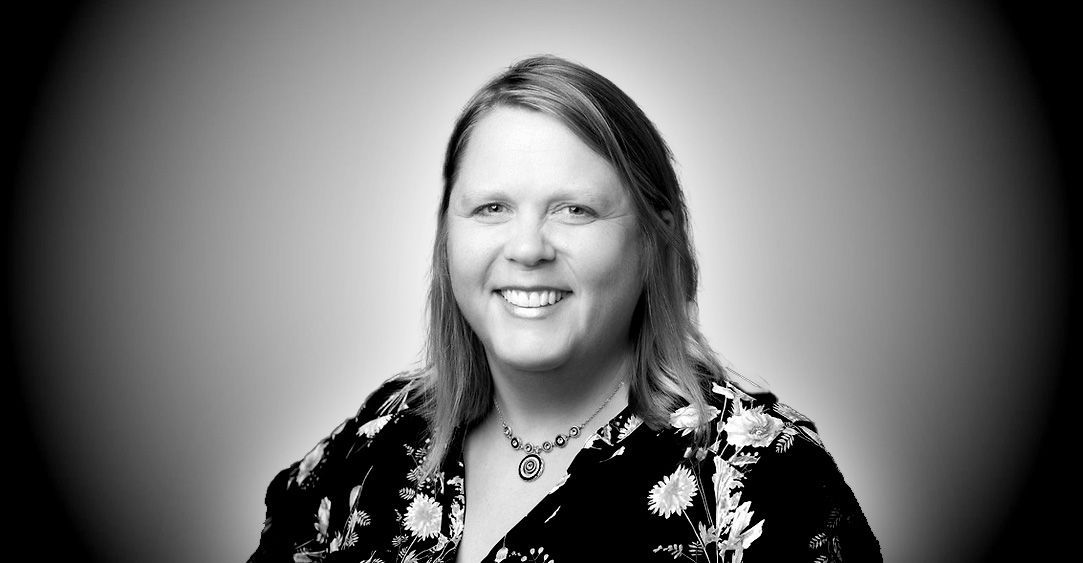 A black and white photo of a woman wearing a floral shirt and necklace.