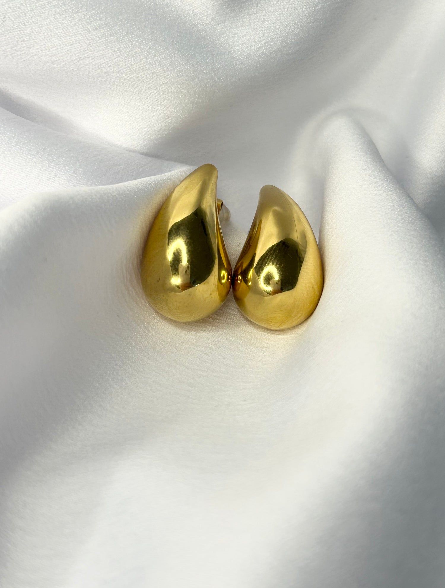 Une paire de boucles d'oreilles en or est posée sur un tissu blanc.