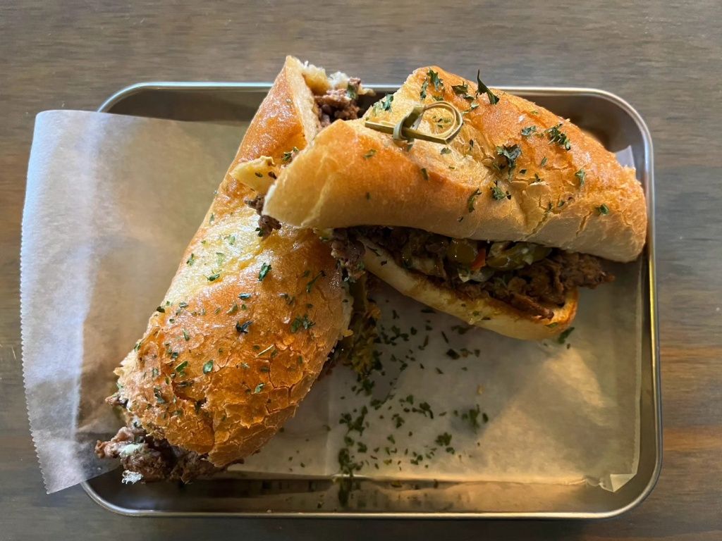 A Toasted Sandwich with Seasoned shaved ribeye topped with provolone and giardiniera olive salad, toasted with garlic aioli