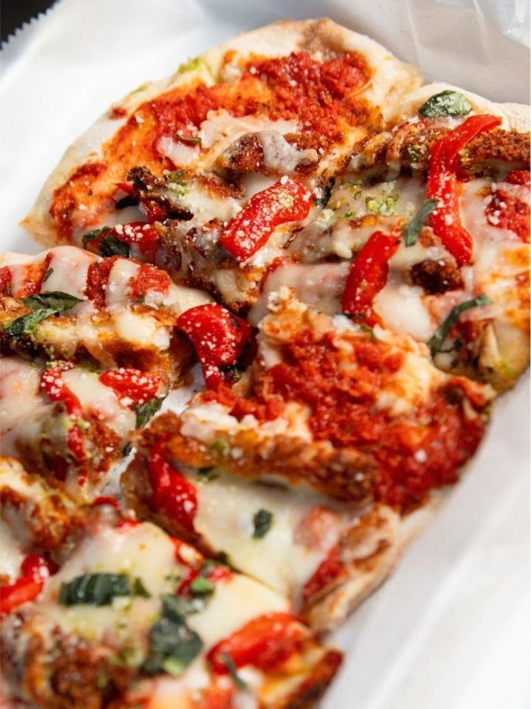 Rectangular pizza slices topped with red sauce, melted mozzarella cheese, roasted red peppers, and fresh basil leaves.