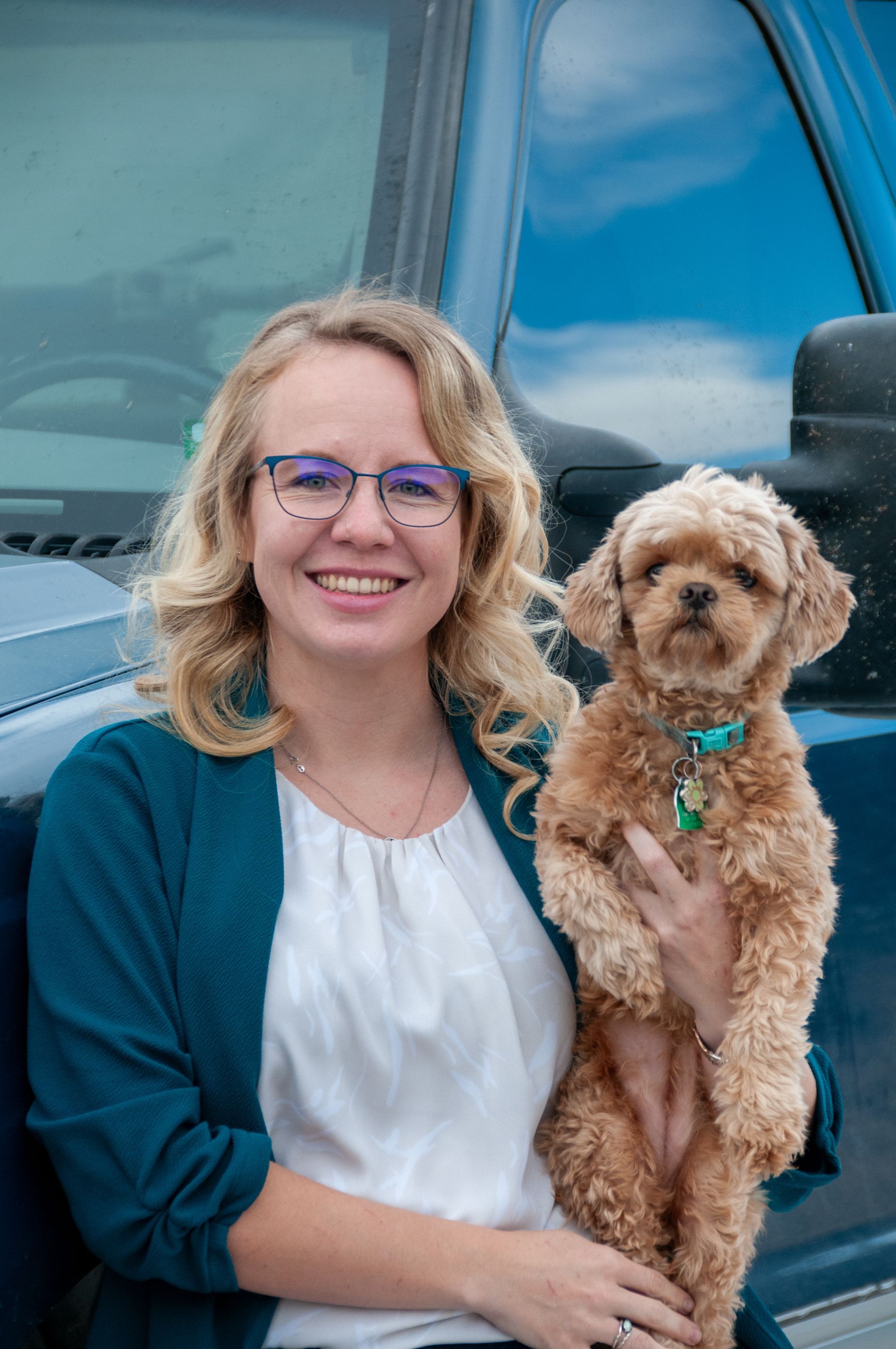 A woman is holding a small brown dog in front of a blue truck.