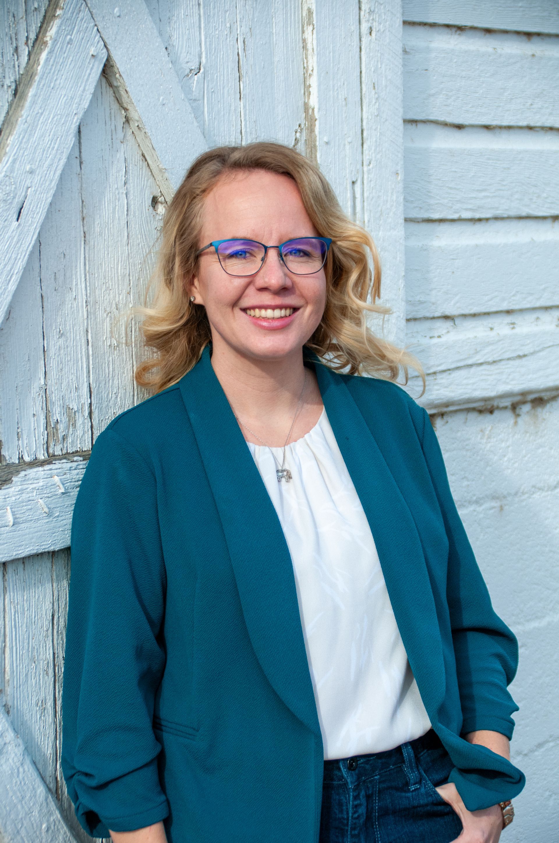 A woman wearing glasses and a blue jacket is standing in front of a white building.