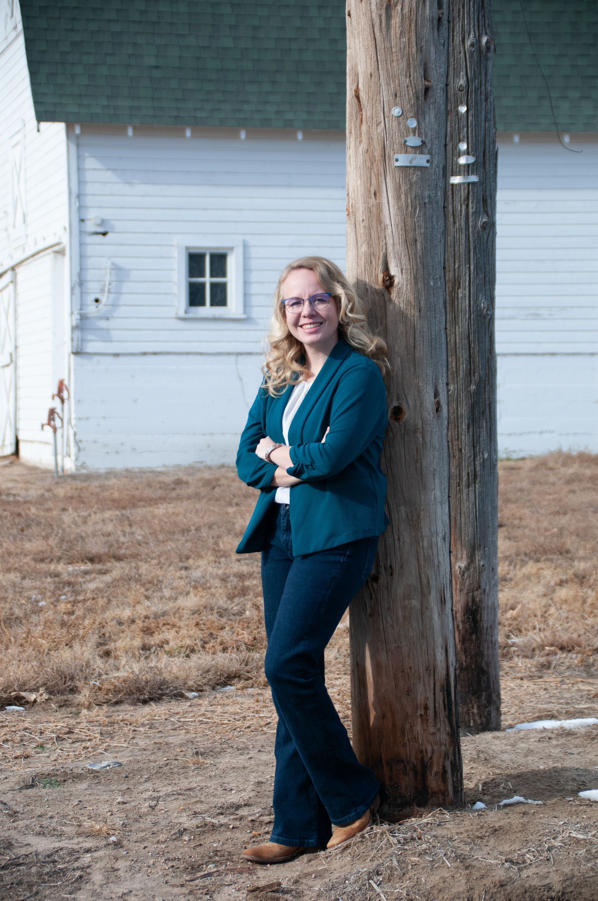 A woman in a blue jacket is leaning against a wooden pole.