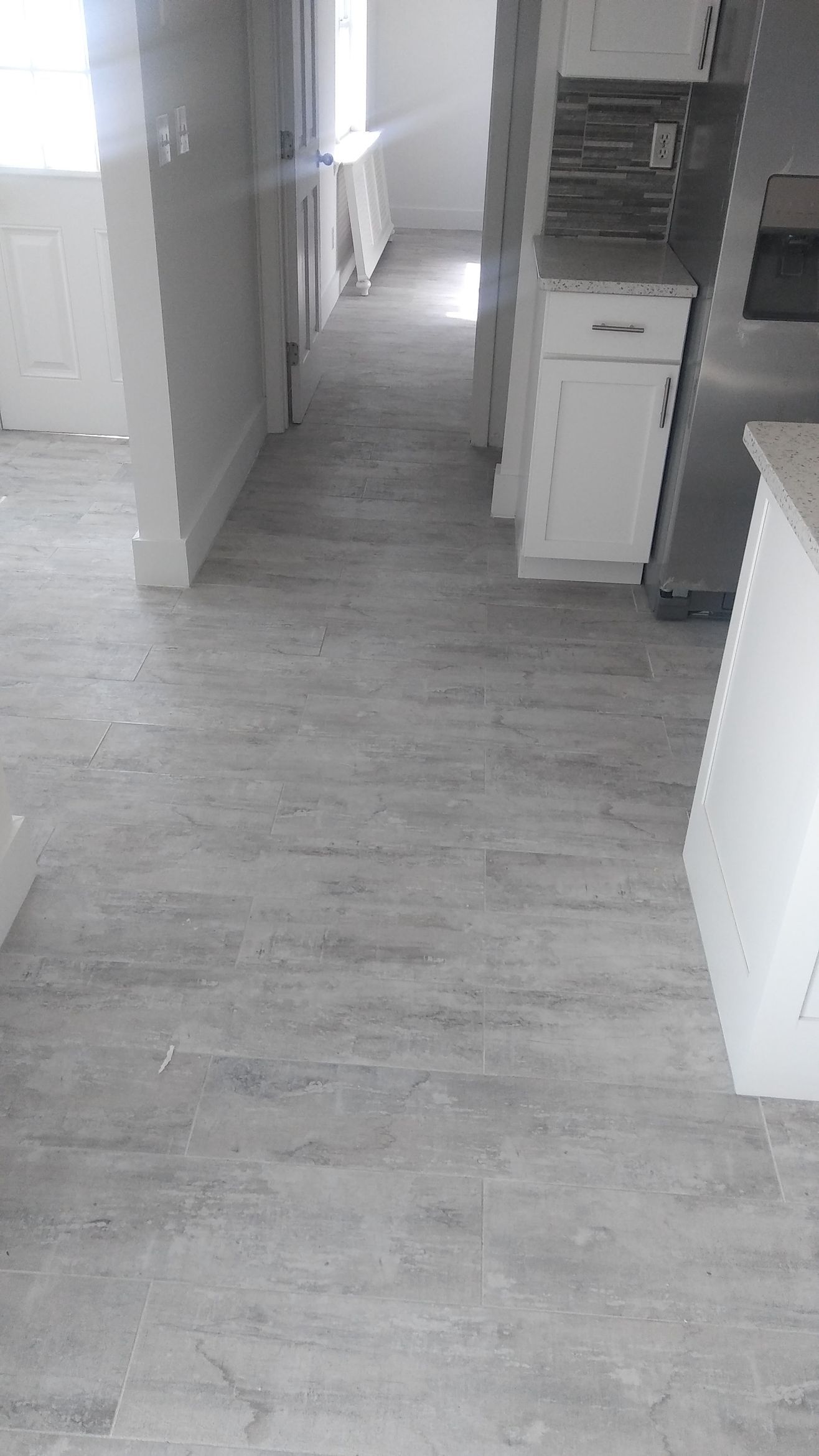 Person installing brown vinyl plank flooring on top of existing light gray flooring.