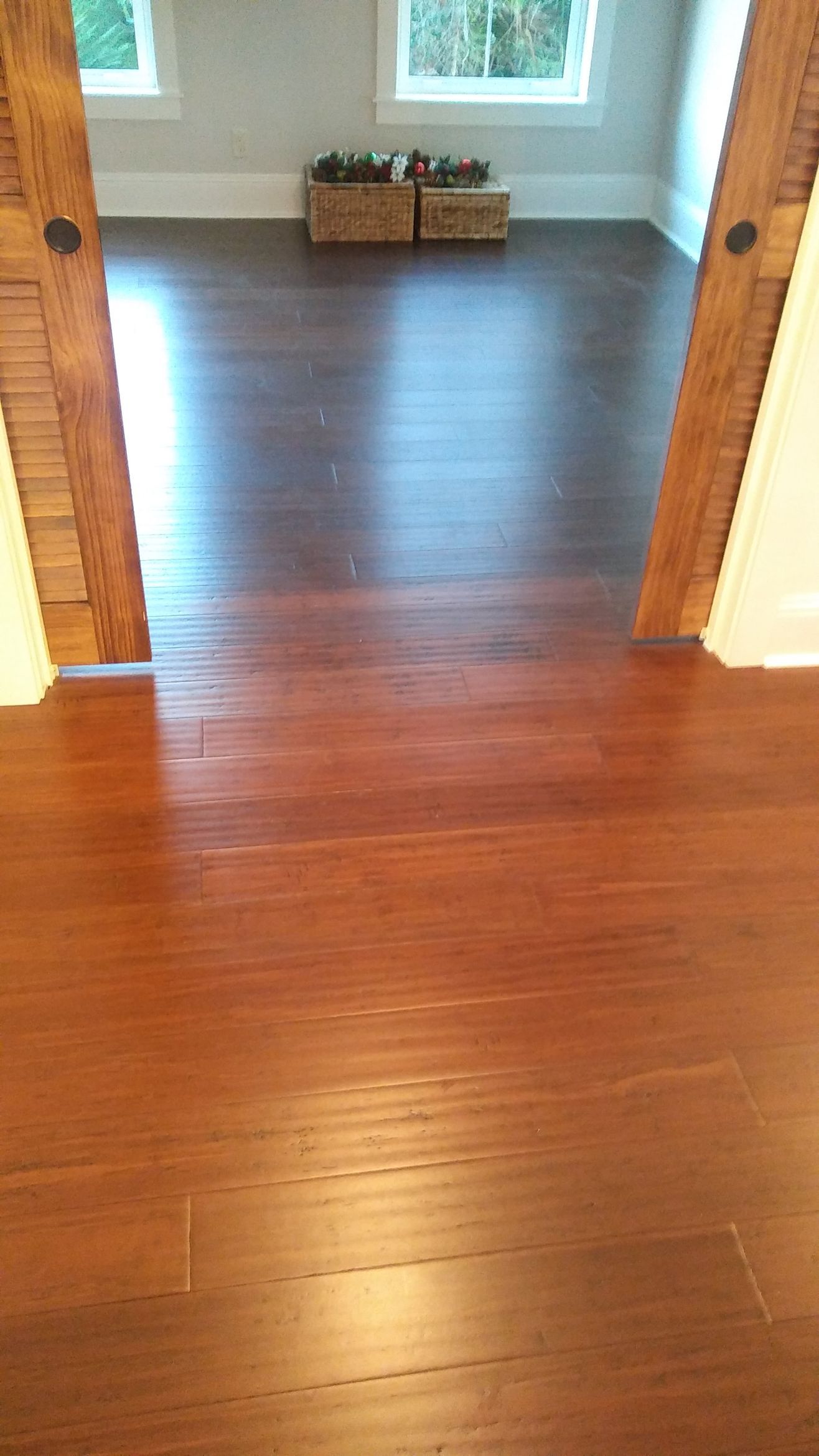 A man installing wood flooring in a room, measuring the planks, wearing work clothes.