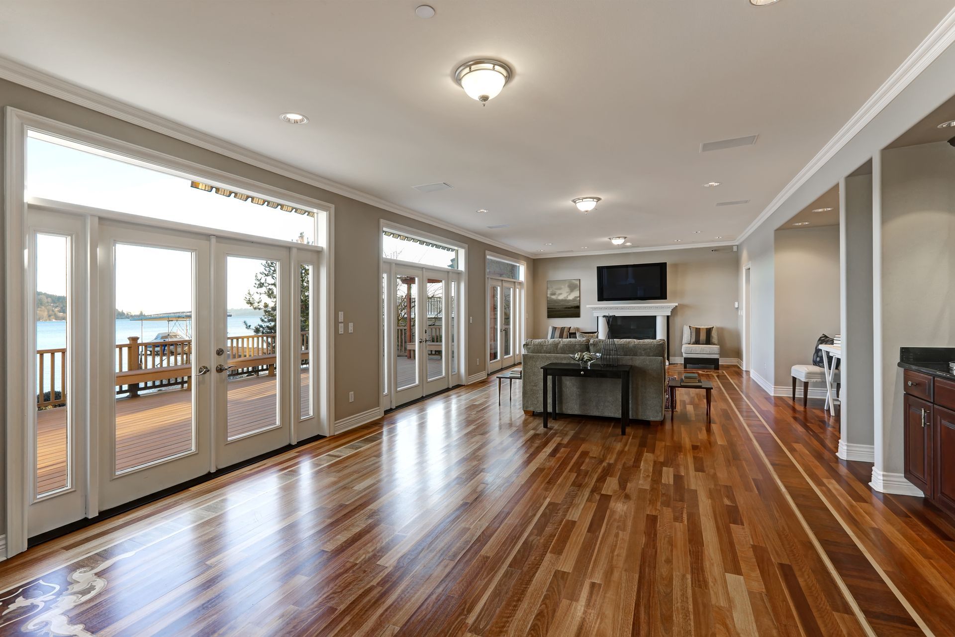 Spacious living room with hardwood floors, large windows, and fireplace; overlooking a deck and water view.