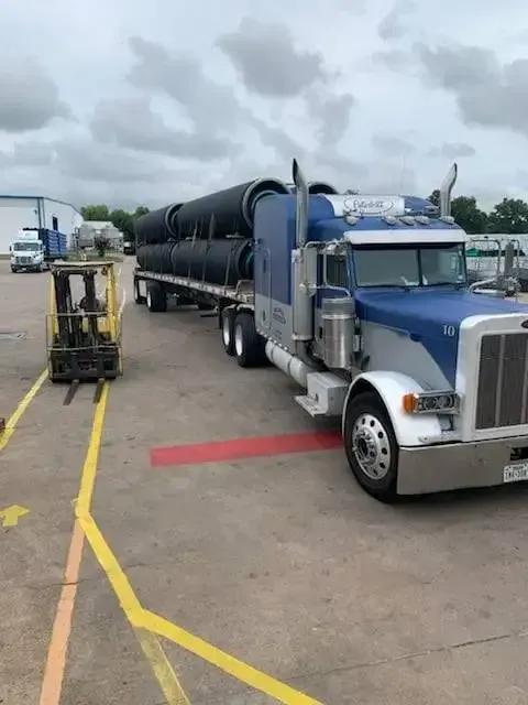 A semi truck with a trailer full of pipes is parked in a parking lot