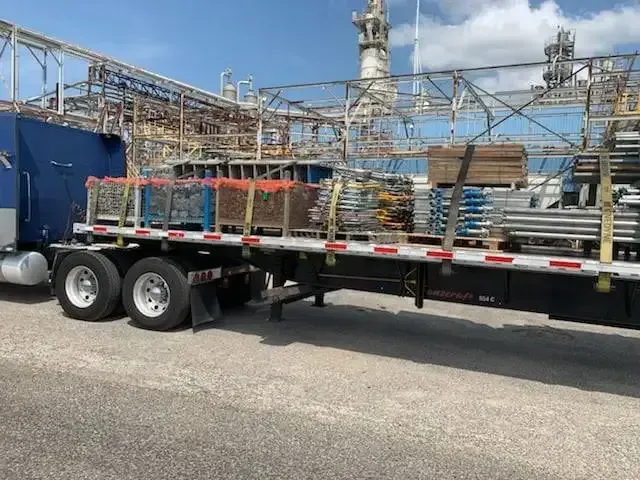 A semi truck with a flatbed trailer is parked in front of a factory.