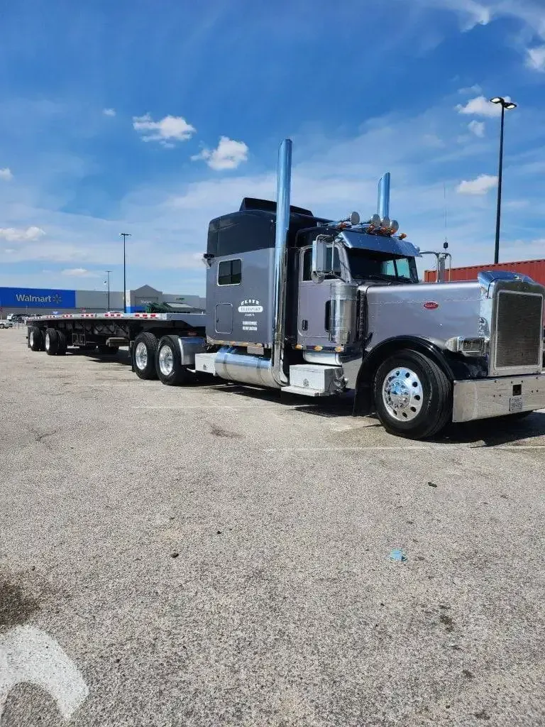 A silver semi truck with a flatbed trailer is parked in a gravel lot.