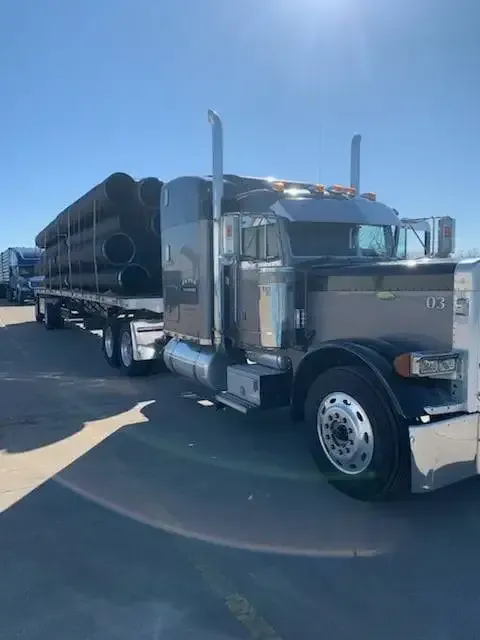 A semi truck with a trailer full of pipes is parked in a parking lot.