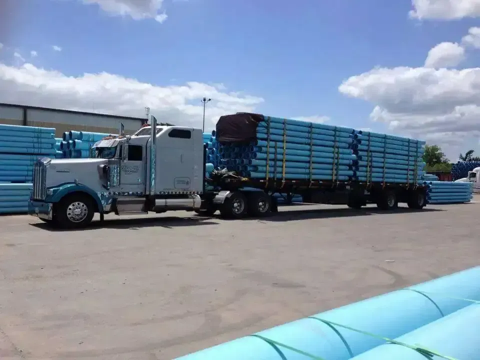 A semi truck is carrying a trailer full of blue pipes.
