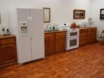 A kitchen with wood cabinets, a white refrigerator, and a white oven against a white wall with two framed pictures.